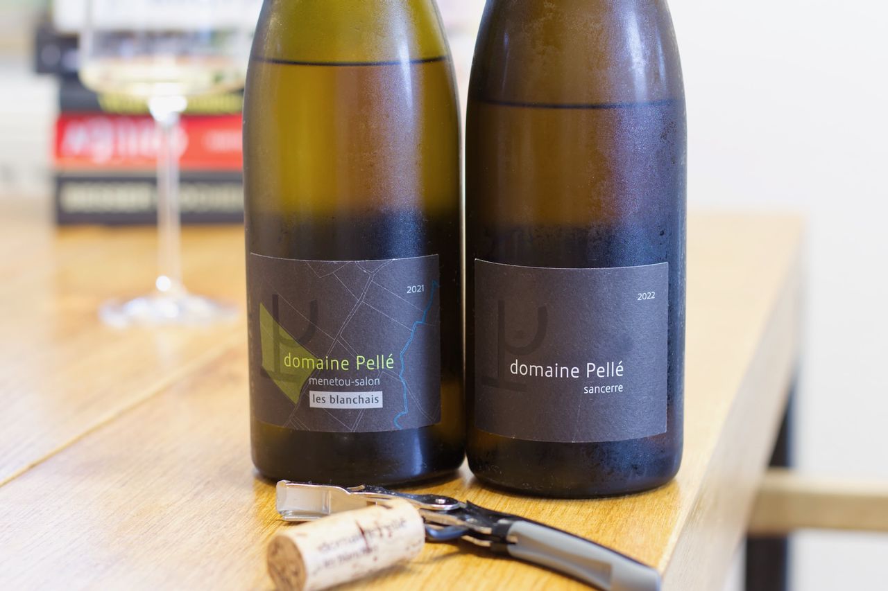 Auf einem Holztisch stehen zwei Flaschen Wein der Domaine Pellé. Ein Sancerre La Croix au Garde und eine Flasche Menetou-Salon Les Blanchais. Im Vordergrund liegt ein Kellnermesser mit den Korken der Flaschen und im Hintergrund steht ein Weinglas vor einem Bücherstapel.