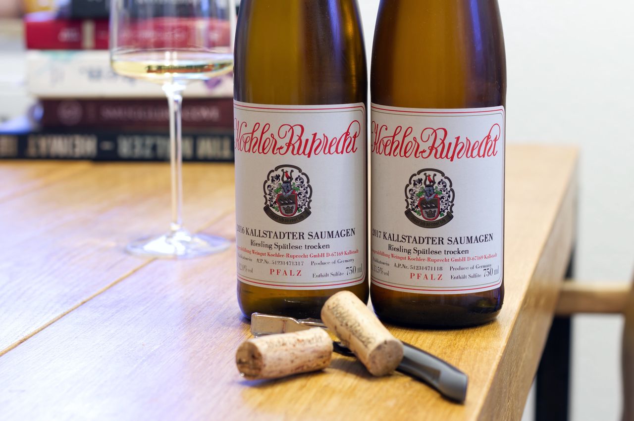 Auf einem Holztisch stehen zwei Flaschen Wein von Köhler-Ruprecht. Im Hintergrund sind ein Weinglas und ein Bücherstapel zu sehen. Vor den Flaschen liegen Korken und Kellnermesser.