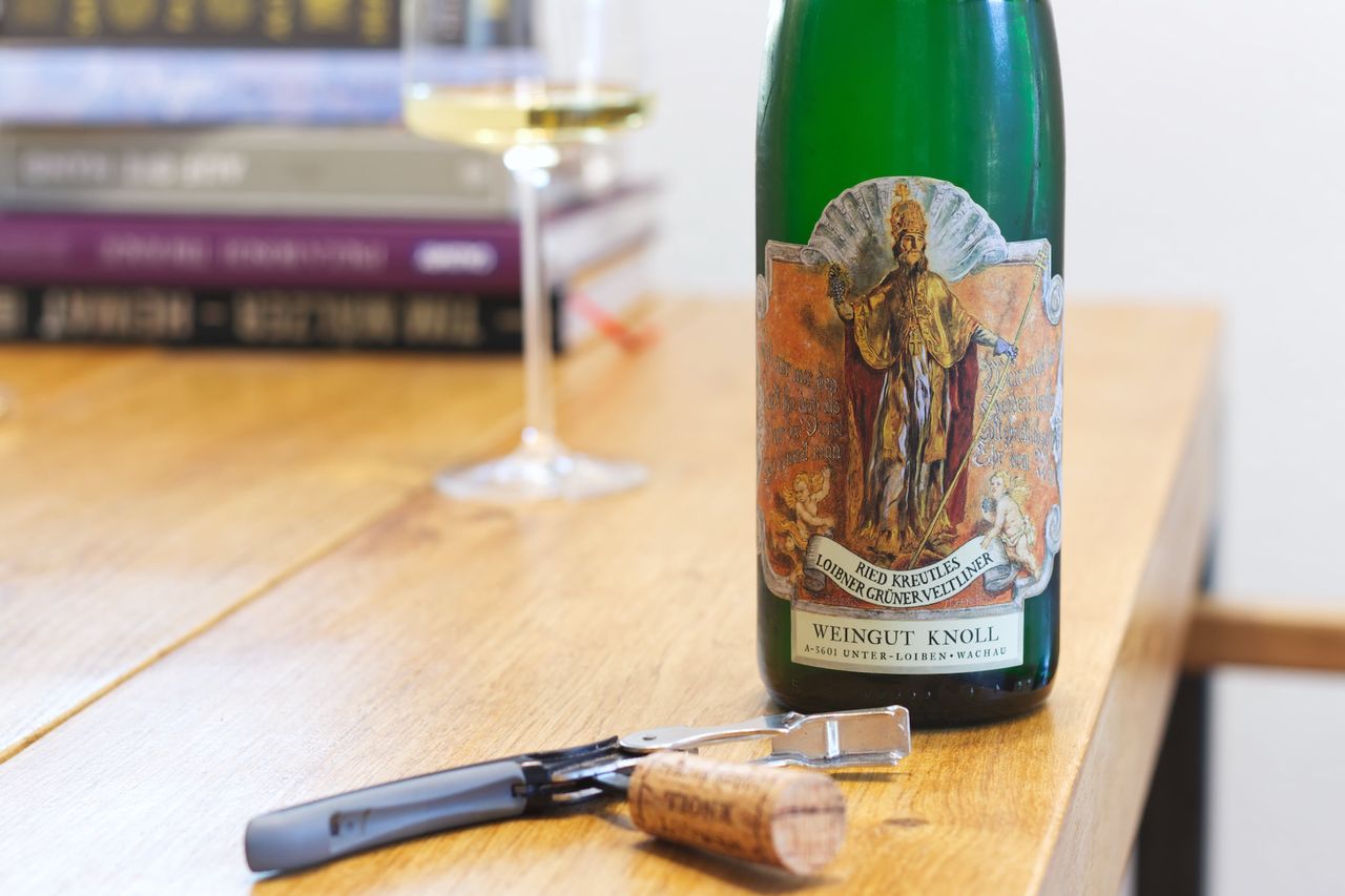 Auf einem Holztisch steht eine Flasche Ried Kreutles Smaragd von Knoll. Im Hintergrund sind ein Weinglas und ein Bücherstapel zu sehen, vor der Flasche liegt der Korken am Kellnermesser.