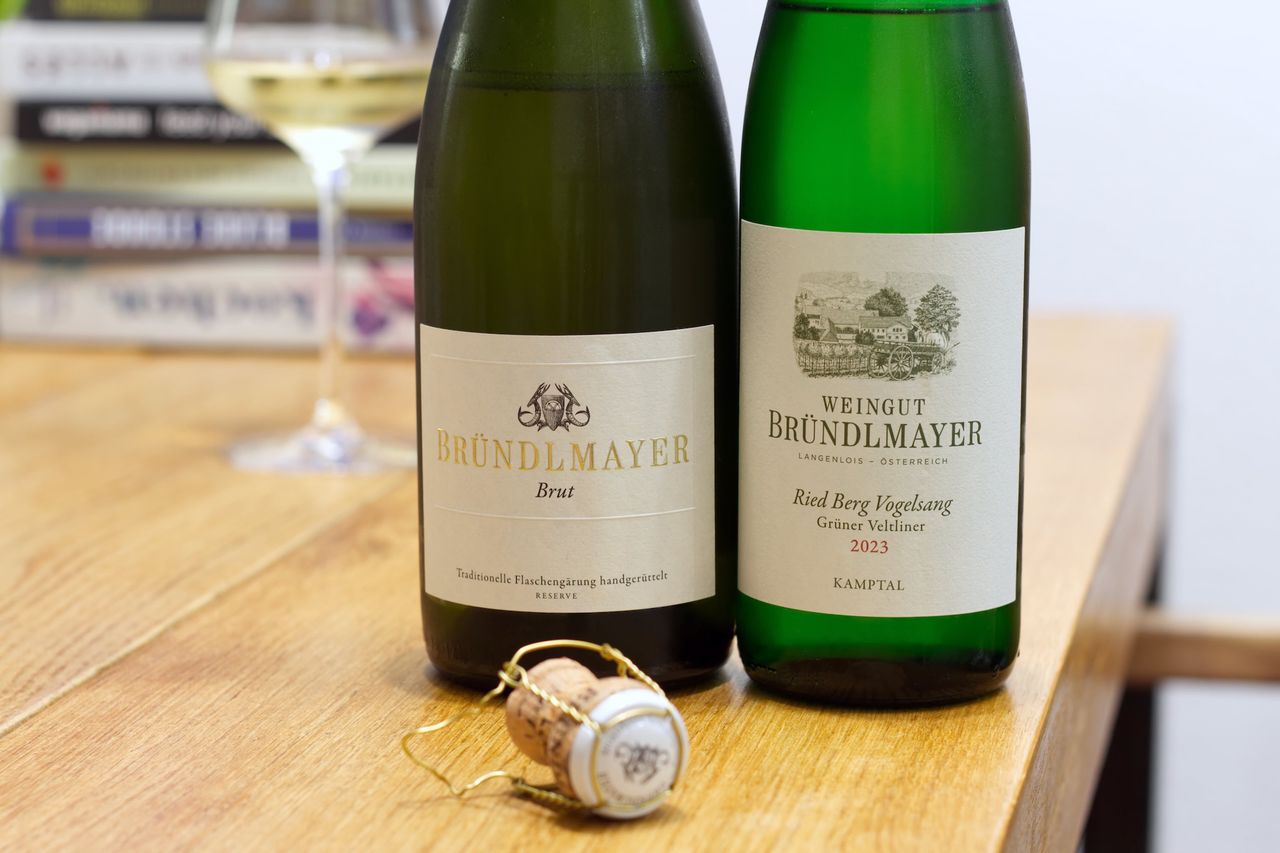 Auf einem Holztisch stehen zwei Flaschen Wein vom Weingut Wachter-Wiesler mit dem Hund auf dem Label. Im Hintergrund sind ein Weinglas und ein Bücherstapel zu sehen. Vor den Flaschen liegt ein Korken am Kellnermesser.