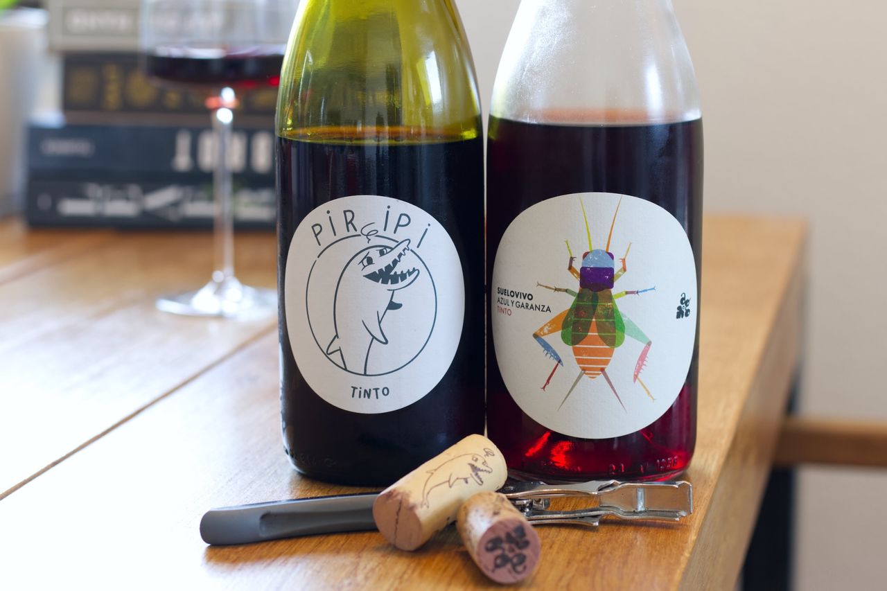 Auf einem Holztisch stehen zwei Flaschen Wein vom Weingut Azul y Garanza. Im Hintergrund sind ein Weinglas und ein Bücherstapel zu sehen. Vor den Flaschen liegen die Korken am Kellnermesser.