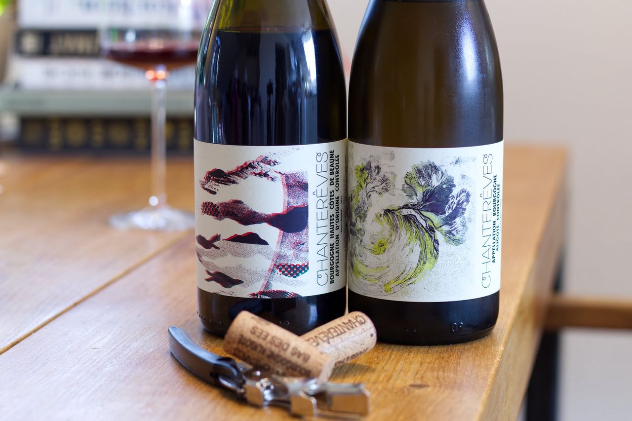 Auf einem Holztisch stehen zwei Flaschen Wein vom Weingut Chanterêves. Im Hintergrund sind ein Weinglas und ein Bücherstapel zu sehen. Vor den Flaschen liegen die Korken am Kellnermesser.