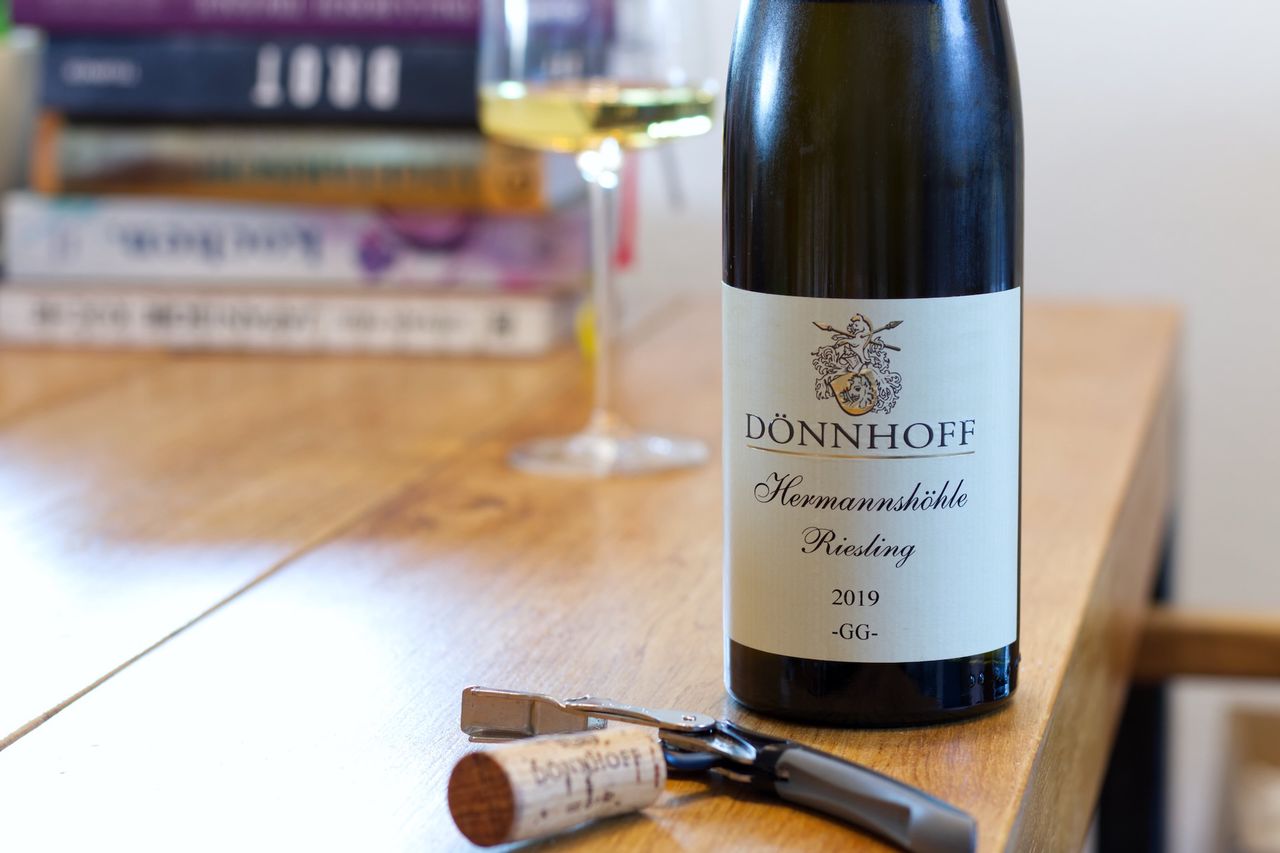 Auf einem Holztisch steht eine Flasche Kirchspiel von Keller. Im Hintergrund sind ein Weinglas und ein Bücherstapel zu sehen, vor der Flasche liegen Korken und Kellnermesser.